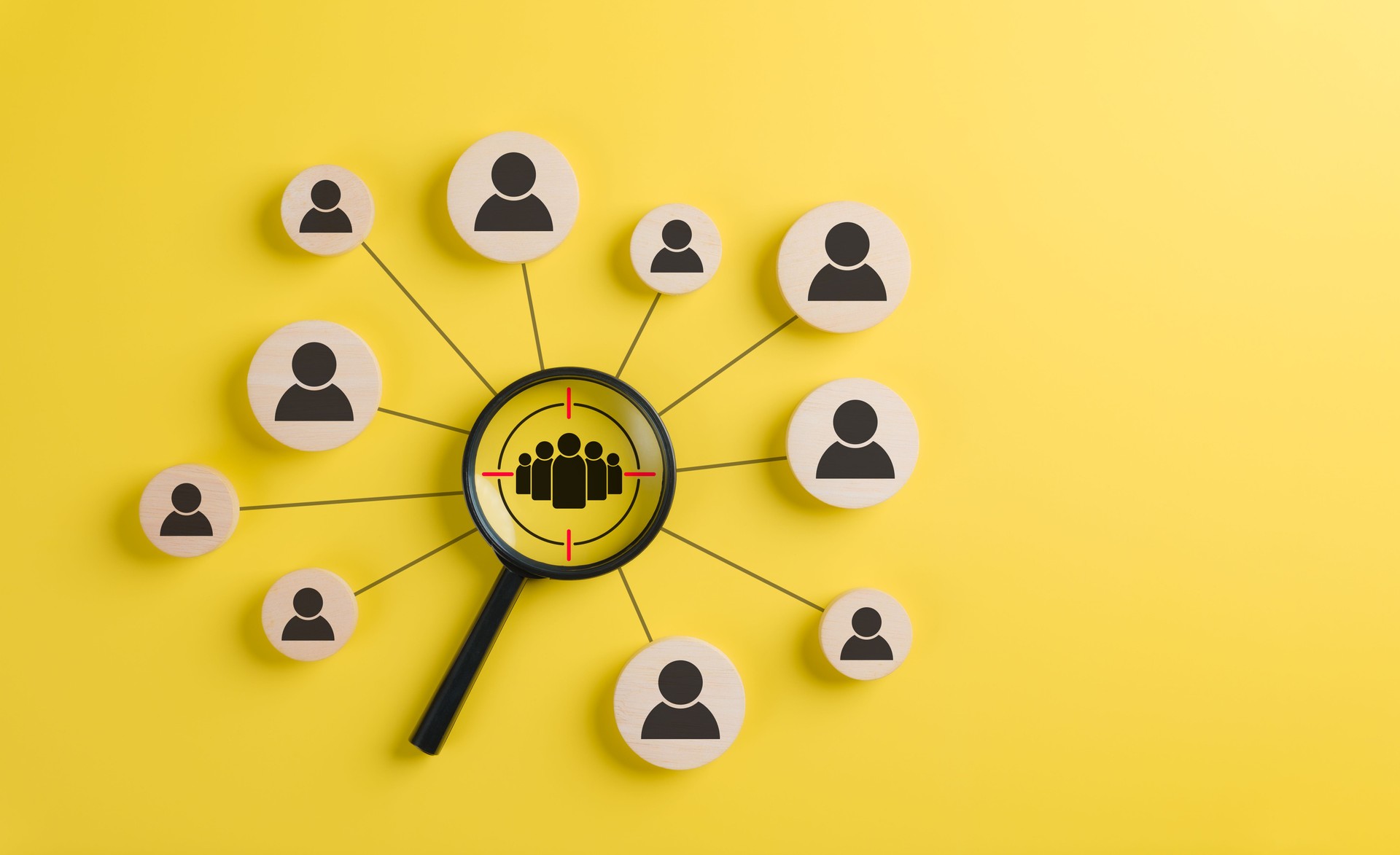 Target audience and customer focus concept. A black magnifying glass highlighting a group of people icons on wooden circles, representing audience targeting, customer focus, digital marketing strategy